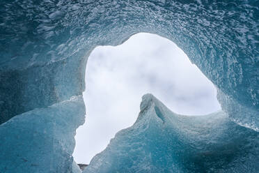 Von unten Eisspitzen, die das Loch in der Höhlendecke umgeben, gegen einen bedeckten grauen Himmel an einem Wintertag im Vatnajokull-Nationalpark in Island - ADSF41069