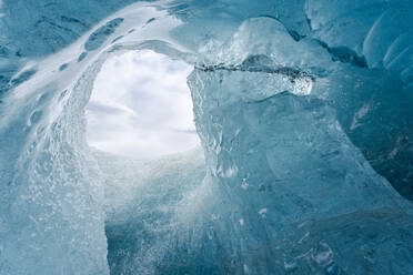 Von unten Eisspitzen, die das Loch in der Höhlendecke umgeben, gegen einen bedeckten grauen Himmel an einem Wintertag im Vatnajokull-Nationalpark in Island - ADSF41071