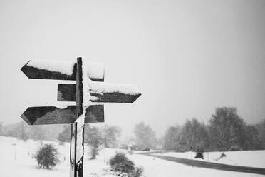 Schwarz und weiß der hölzernen Richtung Straßenschild auf schneebedeckten Feld gegen düsteren bewölkten Himmel auf dem Lande platziert - ADSF41082