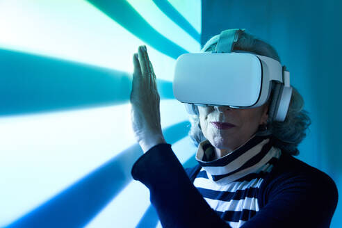 Ältere Frau mit VR-Brille und Kopfhörern, die ein neonfarbenes Netz berührt, während sie den Cyberspace erkundet - ADSF41089