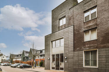 Zeitgenössische mehrstöckige Haus außen gegen Bäume mit Bürgersteig unter blauem Himmel - ADSF41101