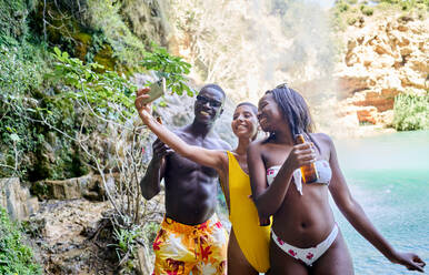 Optimistische hispanische Frau, die ein Selfie mit afroamerikanischen Freunden macht, während sie einen Sommerwochenendtag am Ufer eines Sees verbringen - ADSF41112