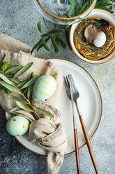 Von oben Besteck für das Osteressen mit Olivenzweigen und Eiern auf einem Vogelnest auf einem konkreten Hintergrund - ADSF41123
