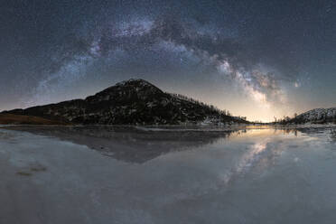 Amazing scenery of glowing stars of Milky Way in night sky over snowy mountain ridge near lake at in Lofoten Islands - ADSF41158