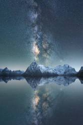 Amazing scenery of glowing stars of Milky Way in night sky over snowy mountain ridge near lake at in Lofoten Islands - ADSF41163