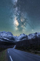 Atemberaubende Landschaft von felsigen Bergkette mit Schnee und leeren Asphaltstraße unter leuchtenden Sternen der Milchstraße in den Nachthimmel in Norwegen bedeckt - ADSF41169