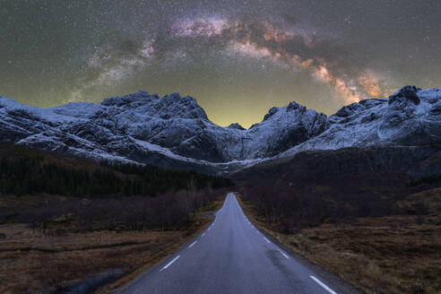 Atemberaubende Landschaft von felsigen Bergkette mit Schnee und leeren Asphaltstraße unter leuchtenden Sternen der Milchstraße in den Nachthimmel in Norwegen bedeckt - ADSF41170