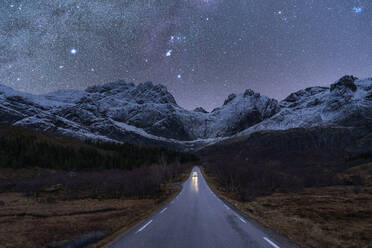 Scenic view of automobile driving on empty mountainous road in winter under night sky glowing stars of Milky Way in Norway - ADSF41171