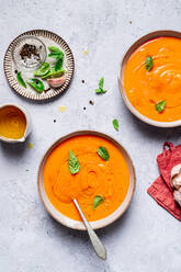 Draufsicht auf Schalen mit Tomatensuppe, die mit Basilikum dekoriert sind und auf dem Tisch neben Soße und Salz mit Knoblauch stehen - ADSF41223