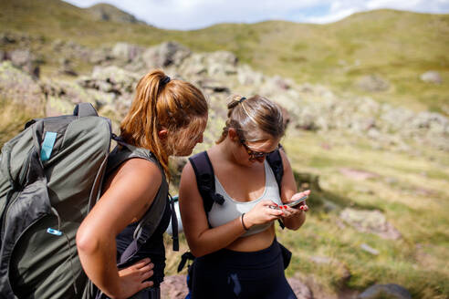 Junge Frauen mit Rucksäcken, die an einem sonnigen Sommertag in den Bergen unterwegs sind und eine GPS-Karte auf ihrem Mobiltelefon lesen - ADSF41243