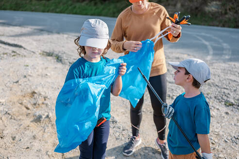 Group of volunteers cleaning up rubbish waste in plastic bags during environmental campaign in countryside - ADSF41246