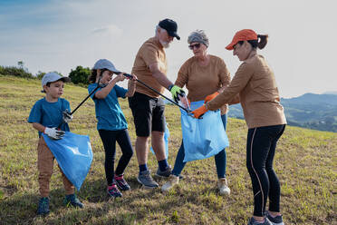 Freiwillige, die während einer Umweltkampagne auf dem Lande den Müll in Müllsäcken mit Stöcken auf der Wiese aufsammeln - ADSF41260