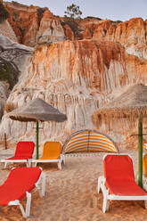 Red loungers located on dry sand sandstone cliff and cloudless blue sky on sunny summer day on Falesia Beach in Algarve, Portugal - ADSF41279