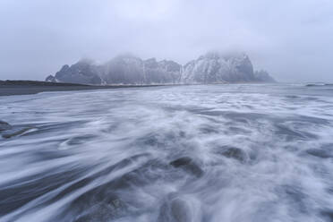 Malerische Szenerie mit starkem stürmischen Meerwasser in der Nähe von rauen felsigen Vestrahorn-Bergformationen an einem nebligen Tag am Strand von Stockness, Island - ADSF41288