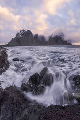 Picturesque scenery of waving sea washing rough shore near high snowy mountains reaching cloudy sky - ADSF41290