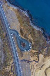 Drohnenansicht einer asphaltierten Straße an der rauen Küste des Meeres an einem grauen Tag in Island - ADSF41296