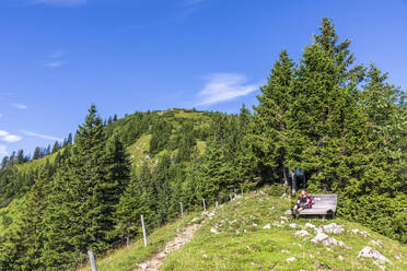 Deutschland, Bayern, Wanderin beim Ausruhen auf einer Bank am Berg - FOF13213