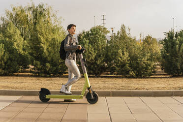 Woman with electric scooter walking on footpath - MGRF00836