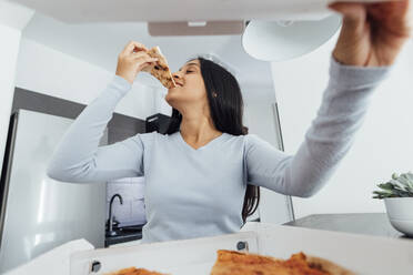 Smiling young woman eating pizza at home - MEUF08623