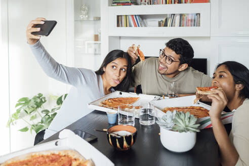 Junge Frau nimmt Selfie durch Handy mit Frau und Mann mit Pizza zu Hause - MEUF08630