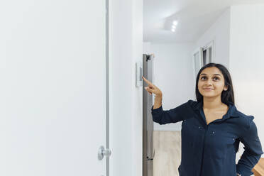 Smiling young woman using smart home device on wall - MEUF08638