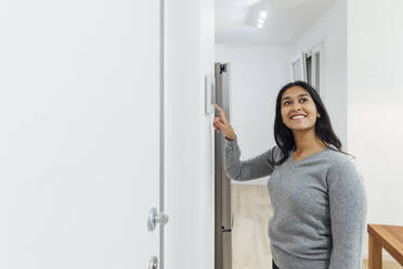 Happy woman using smart home device on wall - MEUF08642