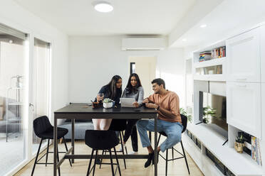 Young woman sharing tablet PC with man and woman at table in living room - MEUF08644