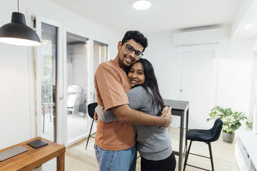 Smiling man embracing happy woman in living room at home - MEUF08655
