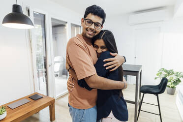 Smiling young man embracing happy woman in living room at home - MEUF08656
