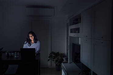 Traurige junge Frau mit Laptop im Wohnzimmer zu Hause - MEUF08673