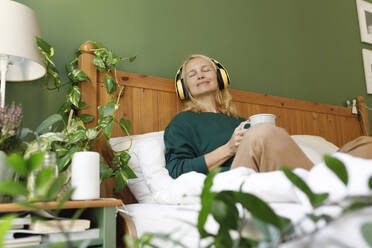 Frau hört Musik über Kopfhörer mit geschlossenen Augen im Schlafzimmer - TYF00452