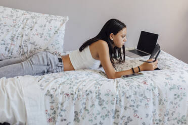 Mädchen mit Tablet-PC auf dem Bett liegend zu Hause - EGHF00668