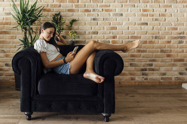 Mädchen, das ein Smartphone benutzt und zu Hause auf einem Sessel sitzt - EGHF00672