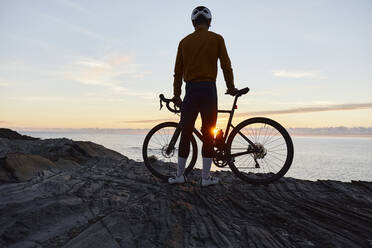 Radfahrer stehend mit Fahrrad vor dem Meer bei Sonnenaufgang - JPTF01106