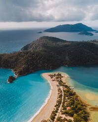 Atemberaubende Drohne Blick auf sandigen Oludeniz Strand in der Nähe türkisfarbenen Meerwasser und grünen Hügeln gegen bewölkten Himmel und Insel am Sommertag in der Türkei - ADSF41359