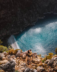 From above drone view of boyfriend and girlfriend hugging each other and kissing while standing on rocks on cliff over blue sea on sunny summer day in Turkey - ADSF41360