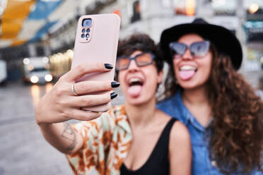 Weichzeichner von glücklichen jungen Freundinnen zeigen Zungen und nehmen Selfie über Smartphone am Wochenende Tag auf der Straße in Madrid, Spanien - ADSF41377