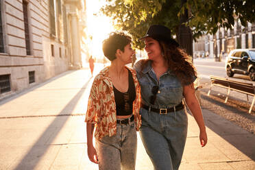 Optimistic young women in stylish clothes smiling while walking on street of Madrid, Spain - ADSF41384