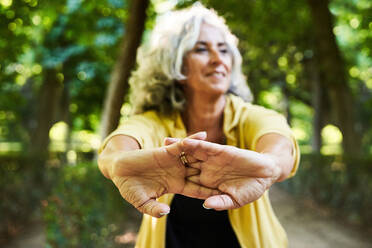 Soft focus of aged female athlete smiling and stretching hands while warming up during fitness workout in park - ADSF41426