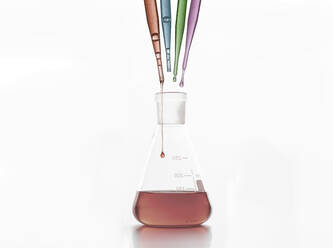 Testtropfen mit Flüssigkeiten über Glas-Laborkolben auf dem Schreibtisch vor weißem Hintergrund - ADSF41445