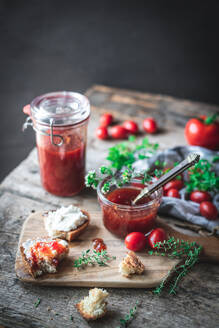 Kleines Glas mit frischer Tomatenmarmelade neben karierter Serviette und grünen Kräutern auf dem Holztisch - ADSF41451