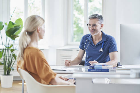Glücklicher Arzt im Gespräch mit einem Patienten in einer Arztpraxis - RORF03070