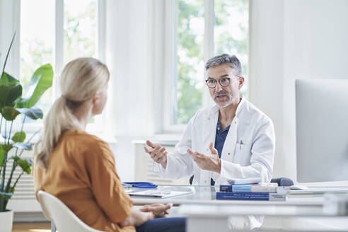 Arzt im Gespräch mit einem am Schreibtisch sitzenden Patienten in einer Arztpraxis - RORF03076