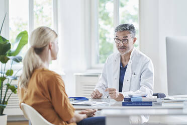 Mature doctor discussing with patient sitting at medical practice - RORF03077