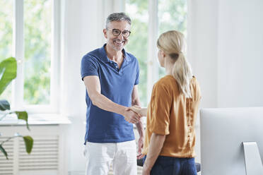 Happy mature doctor shaking hands with patient in medical practice - RORF03081