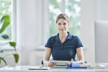 Smiling doctor sitting with tablet PC at desk - RORF03093