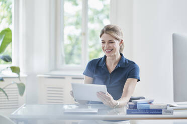 Happy female doctor using tablet PC at desk in medical practice - RORF03098