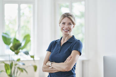 Happy female doctor with arms crossed standing in medical practice - RORF03104