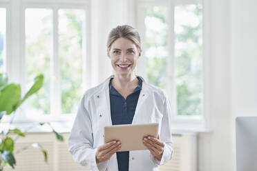 Happy female doctor standing with tablet PC at medical practice - RORF03116