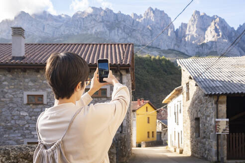 Spain, Castile and Leon, Posada de Valdeon, Female tourist taking photos of stone houses in Picos de Europa - MMPF00525